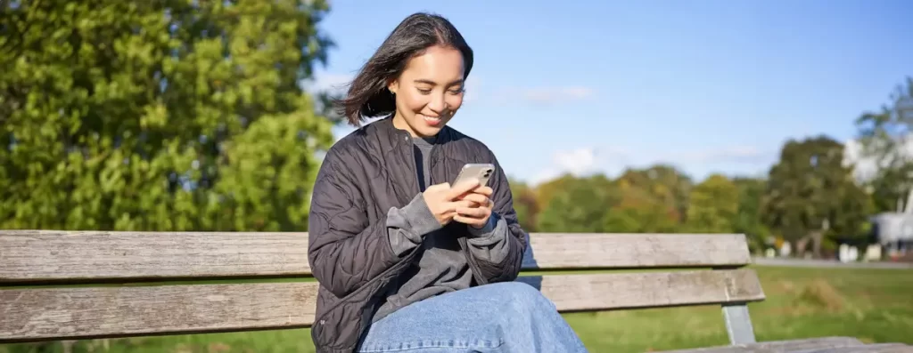 Vrouw gebruikt smartphone op parkbankje.