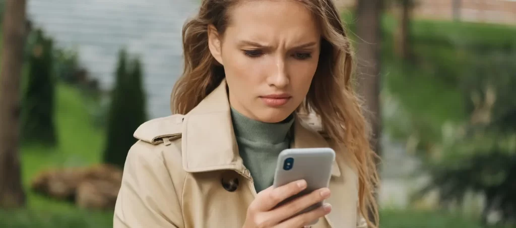 Vrouw bezorgd kijkend naar smartphone buitenshuis.