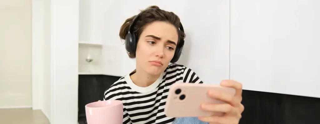 Vrouw met koptelefoon kijkt naar smartphone.