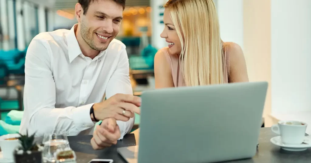 Twee verliefde collega's lachen bij laptop in café.