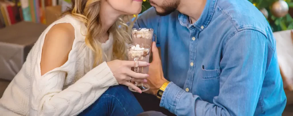 Koppel geniet van chocolademelk bij kerstboom.